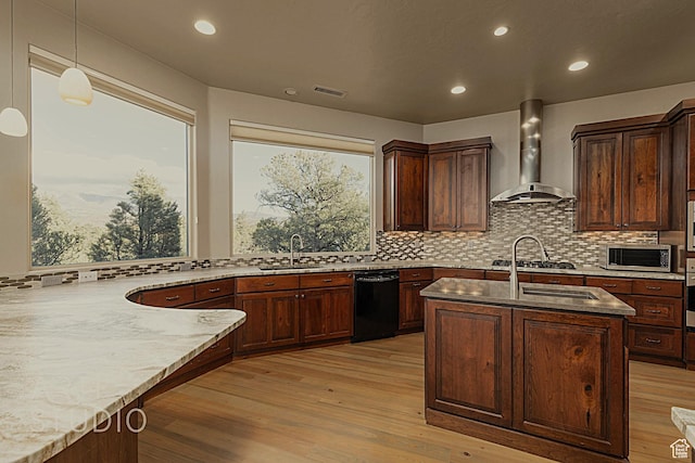 kitchen with pendant lighting, appliances with stainless steel finishes, light stone counters, wall chimney exhaust hood, and light wood-type flooring