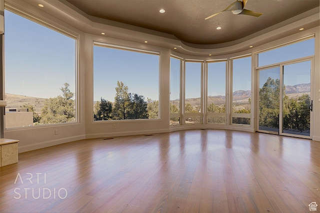 unfurnished sunroom with ceiling fan, a mountain view, a raised ceiling, and a wealth of natural light