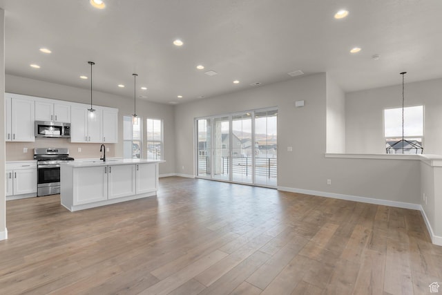 kitchen featuring pendant lighting, light wood-type flooring, stainless steel appliances, and white cabinetry