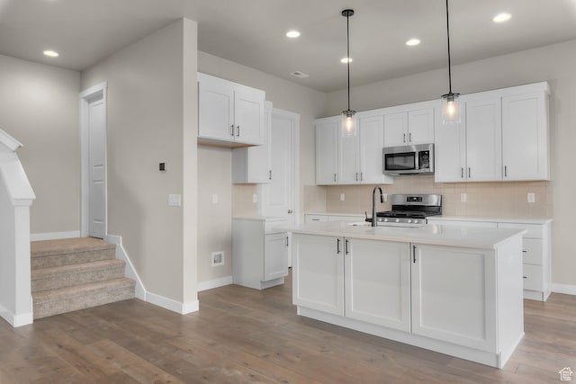 kitchen with white cabinetry, a center island with sink, hanging light fixtures, and appliances with stainless steel finishes