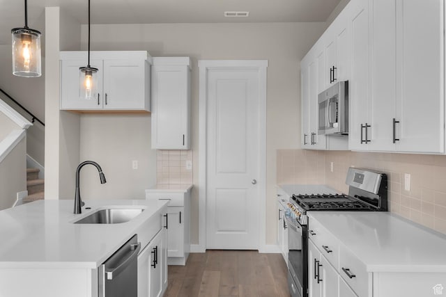 kitchen featuring white cabinetry, sink, hanging light fixtures, stainless steel appliances, and backsplash