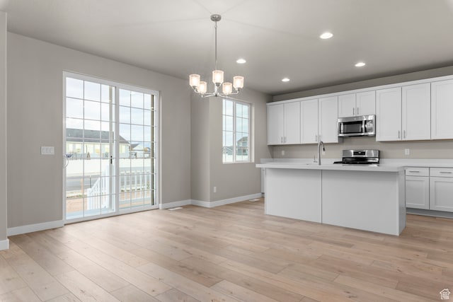 2616 N 3020 W, Clinton, UT 84015 - kitchen featuring appliances with stainless steel finishes, light wood-type flooring, a kitchen island with sink, decorative light fixtures, and white cabinets