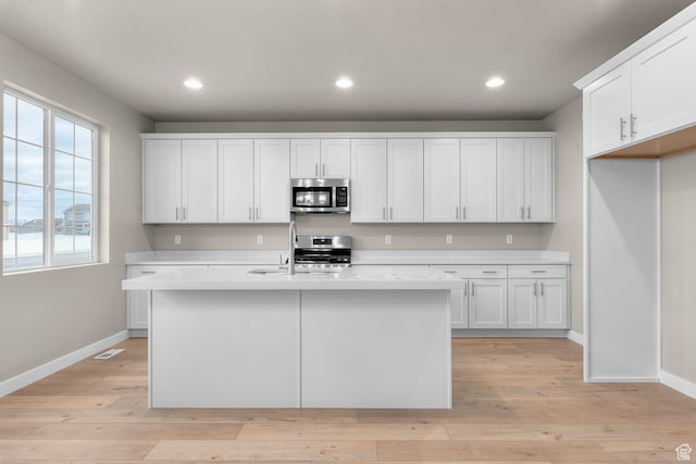 2616 N 3020 W, Clinton, UT 84015 - kitchen with white cabinets, appliances with stainless steel finishes, light hardwood / wood-style floors, and an island with sink