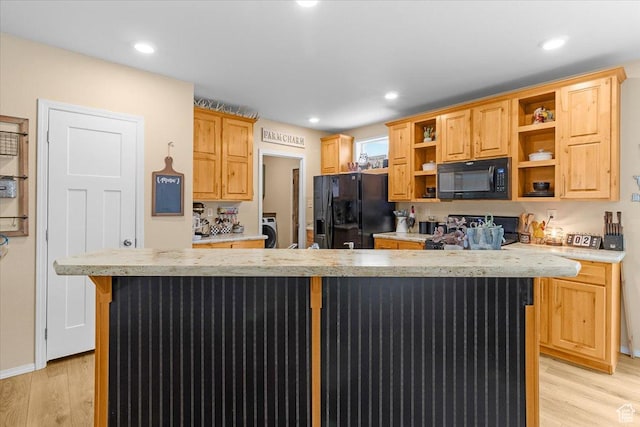 kitchen featuring light brown cabinetry, a kitchen island, black appliances, and light wood-type flooring