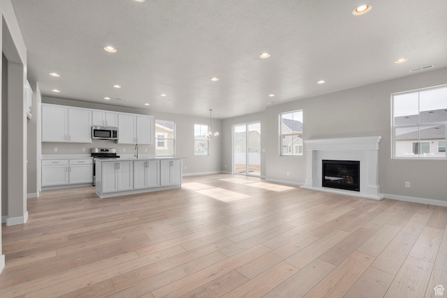 1839 S 2475 W, West Haven, UT 84401 - unfurnished living room with a textured ceiling, light wood-type flooring, a notable chandelier, and sink