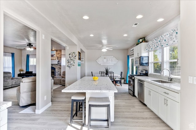 kitchen featuring appliances with stainless steel finishes, a ceiling fan, a stone fireplace, and a sink