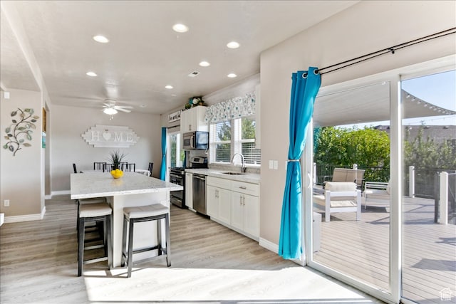 kitchen with a sink, stainless steel appliances, light wood-style floors, a kitchen island, and white cabinets