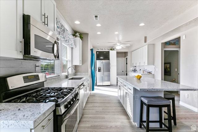 kitchen featuring a textured ceiling, light wood-style flooring, a sink, appliances with stainless steel finishes, and a center island