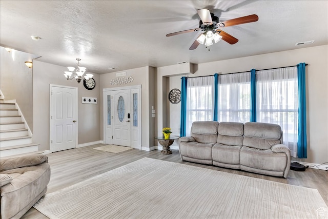 living area with stairs, light wood-style floors, ceiling fan with notable chandelier, baseboards, and visible vents