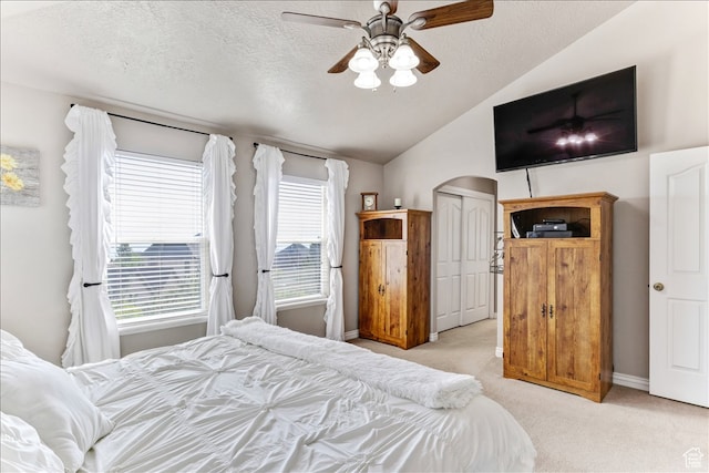 bedroom featuring a textured ceiling, light colored carpet, baseboards, vaulted ceiling, and a ceiling fan