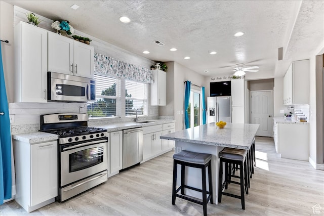 kitchen featuring appliances with stainless steel finishes, a kitchen island, a sink, visible vents, and a textured ceiling