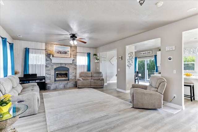 living room featuring light wood finished floors, a fireplace, a ceiling fan, baseboards, and a textured ceiling