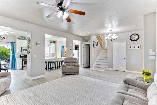 living room with stairway, light wood-style flooring, baseboards, a textured ceiling, and ceiling fan with notable chandelier