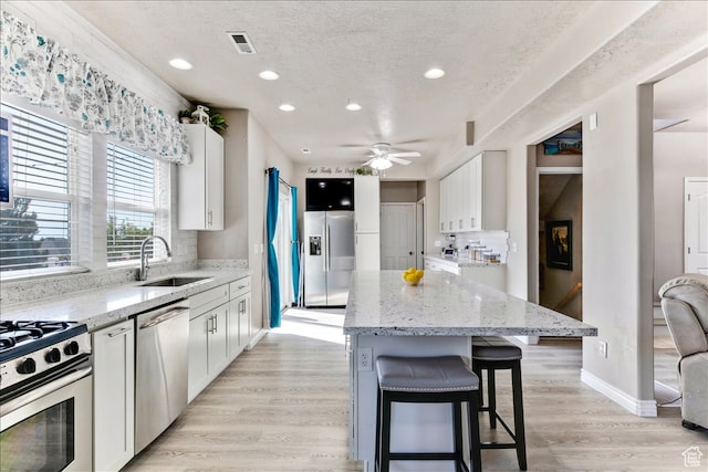 kitchen featuring white cabinets, a sink, ceiling fan, stainless steel appliances, and a kitchen island