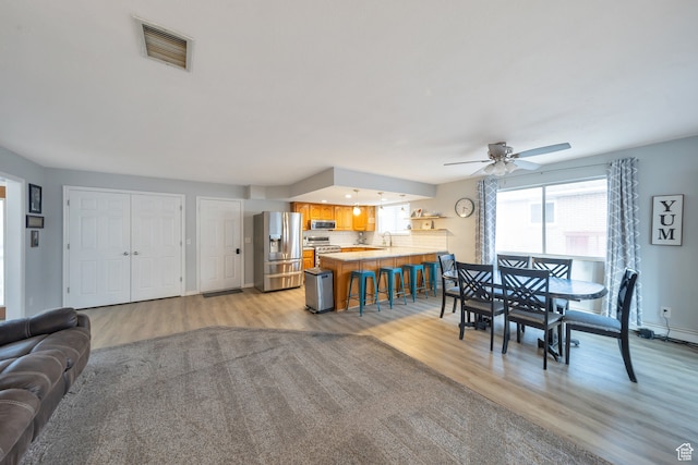 dining space featuring ceiling fan, sink, and light wood-type flooring