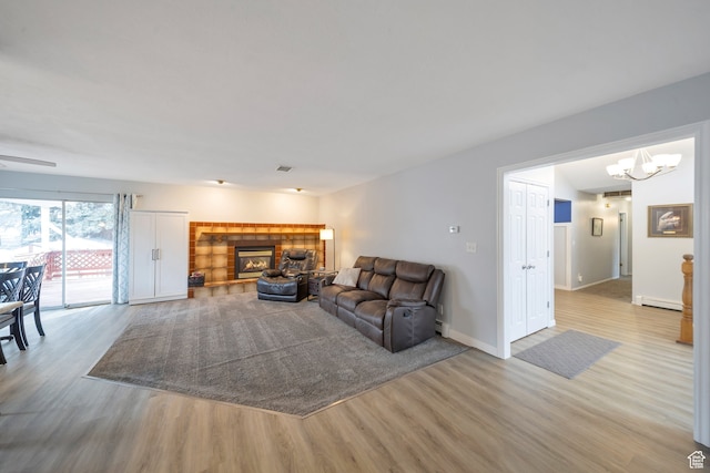 living room featuring a tiled fireplace, light hardwood / wood-style flooring, a baseboard radiator, and an inviting chandelier