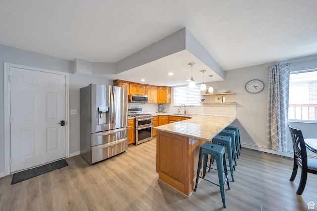 kitchen featuring kitchen peninsula, stainless steel appliances, light hardwood / wood-style flooring, hanging light fixtures, and a breakfast bar area