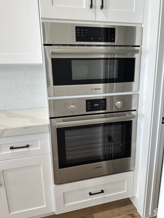 interior details with stainless steel double oven, dark hardwood / wood-style flooring, white cabinetry, and light stone counters