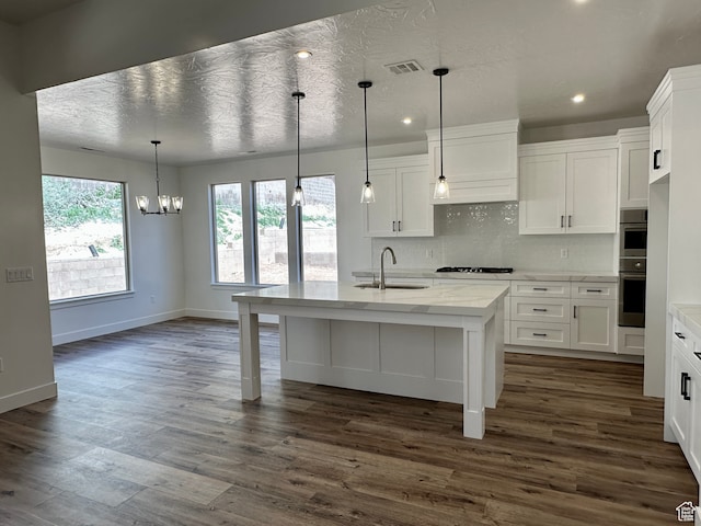 kitchen with pendant lighting, a breakfast bar, white cabinets, sink, and an island with sink