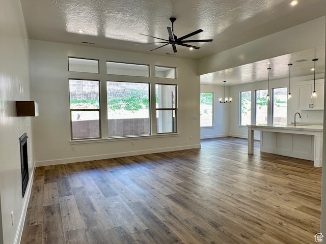 unfurnished living room featuring a textured ceiling, dark hardwood / wood-style flooring, ceiling fan with notable chandelier, and sink