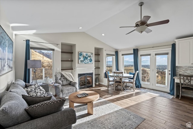 living room featuring built in shelves, lofted ceiling, ceiling fan, and dark wood-type flooring