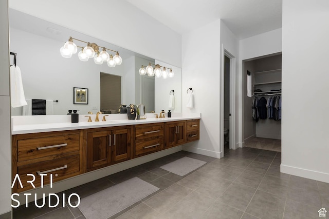 full bath featuring double vanity, baseboards, tile patterned flooring, a walk in closet, and a sink
