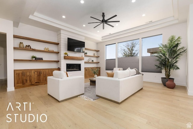 living room featuring light wood-style flooring, a fireplace, visible vents, baseboards, and a raised ceiling