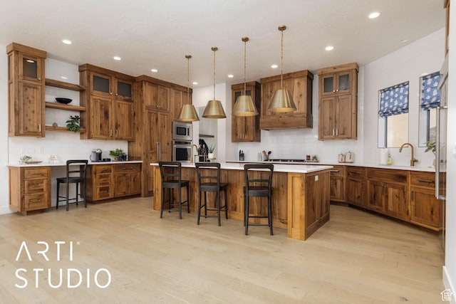kitchen with light countertops, hanging light fixtures, brown cabinetry, and a kitchen island with sink