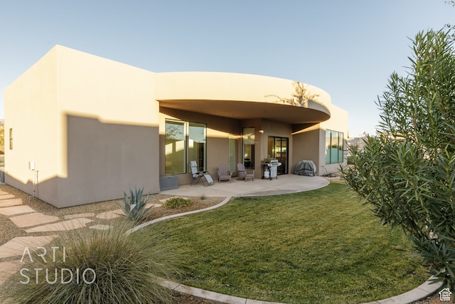 back of property featuring stucco siding, a lawn, and a patio