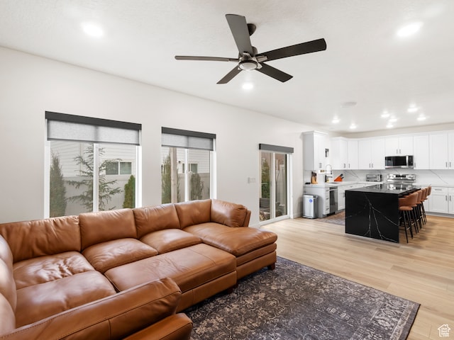 living room with ceiling fan, plenty of natural light, sink, and light wood-type flooring