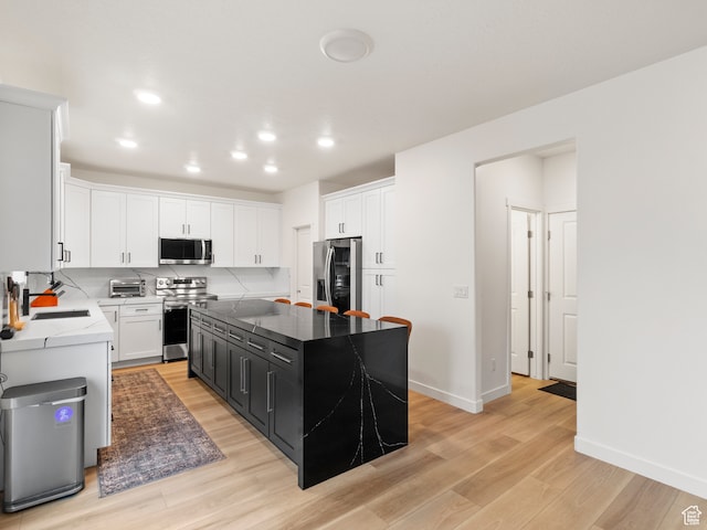 kitchen with white cabinetry, sink, stainless steel appliances, a kitchen island, and light wood-type flooring