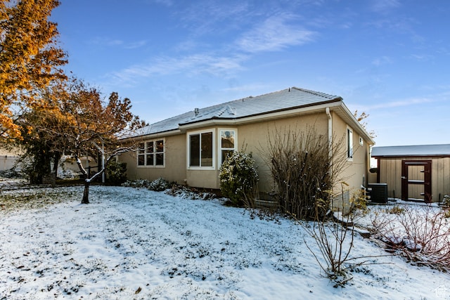 snow covered rear of property with a storage unit and central AC unit