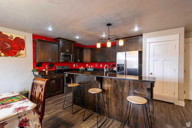 279 W 20 N, Hyrum, UT 84319 - kitchen featuring dark brown cabinets, stainless steel appliances, a kitchen island with sink, dark wood-type flooring, and pendant lighting