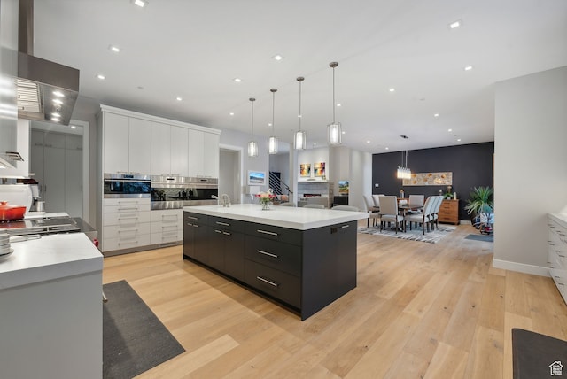 kitchen featuring white cabinets, light wood-type flooring, decorative light fixtures, and a large island
