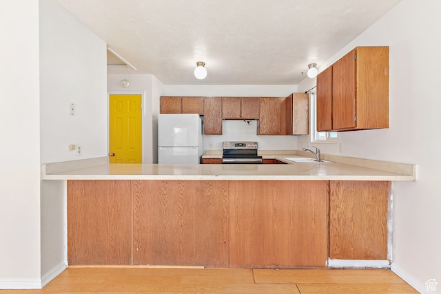 kitchen with kitchen peninsula, stainless steel electric stove, sink, white refrigerator, and light hardwood / wood-style floors