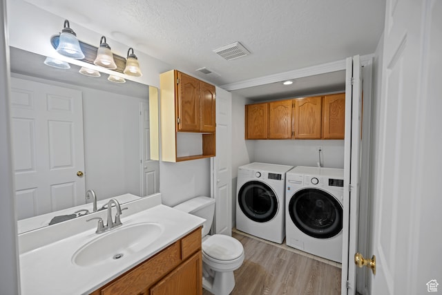 laundry area with cabinets, sink, light hardwood / wood-style flooring, independent washer and dryer, and a textured ceiling