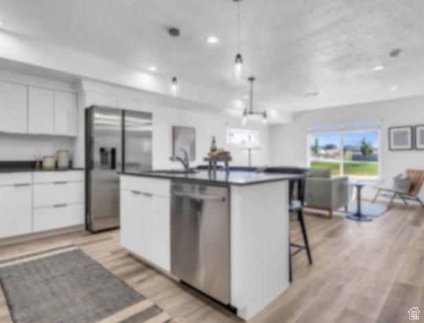 kitchen featuring a kitchen island with sink, white cabinets, light hardwood / wood-style flooring, appliances with stainless steel finishes, and decorative light fixtures