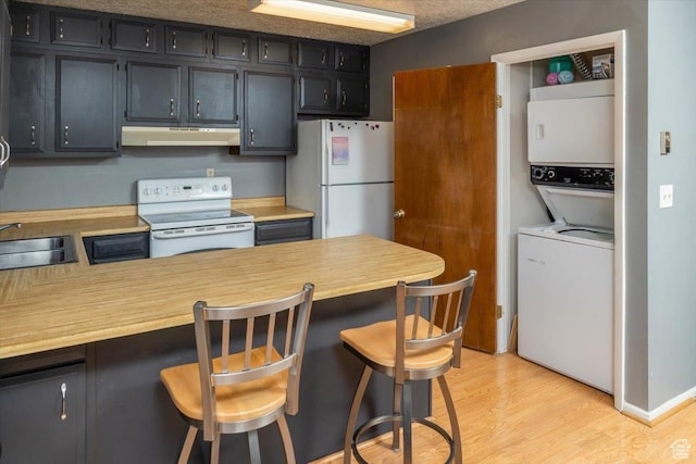 281 W 600 N Unit 4, Logan, UT 84321 - kitchen with stacked washing maching and dryer, light hardwood / wood-style flooring, a textured ceiling, white appliances, and a breakfast bar
