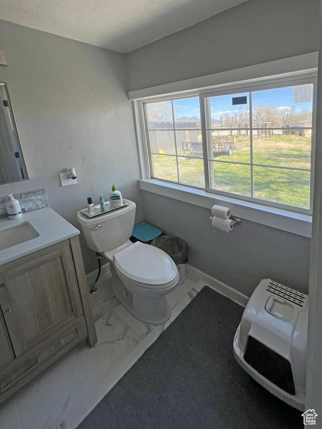 half bathroom featuring vanity, toilet, marble finish floor, and baseboards