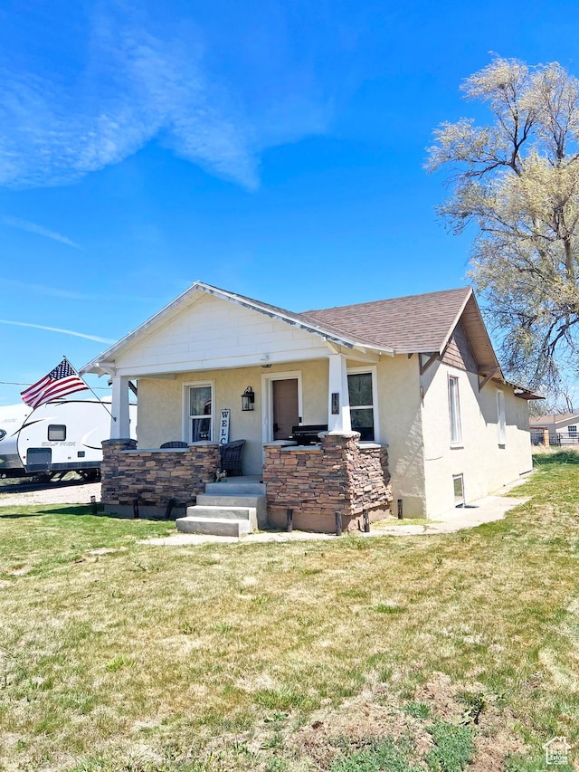 bungalow-style home with a front lawn, stucco siding, and stone siding