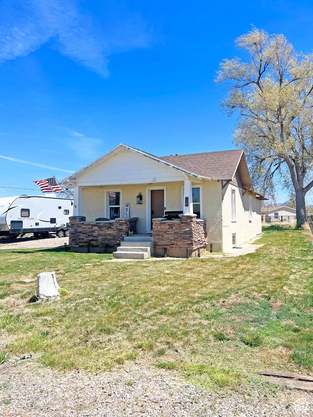 bungalow with stucco siding, a front yard, and stone siding