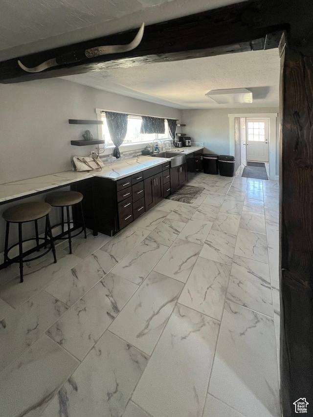 kitchen with a breakfast bar, marble finish floor, light countertops, and a sink