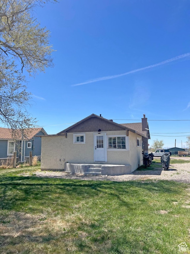 back of house with stucco siding and a lawn
