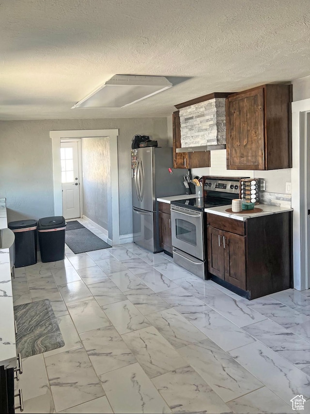 kitchen with appliances with stainless steel finishes, a textured ceiling, marble finish floor, and baseboards