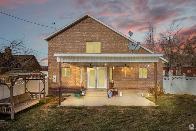 back house at dusk with a yard, a patio, and french doors