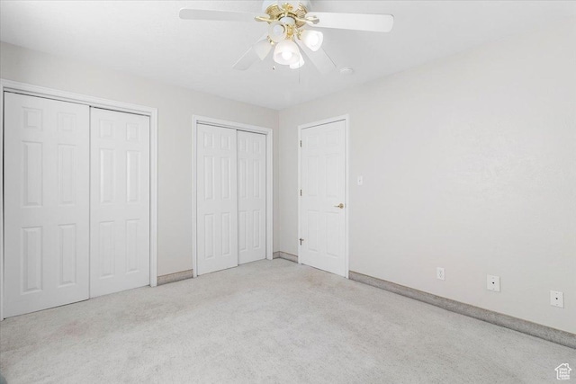 unfurnished bedroom featuring ceiling fan, light colored carpet, and two closets