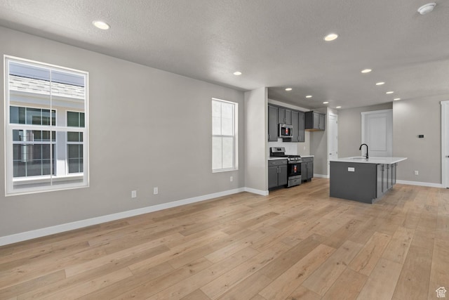 interior space featuring a kitchen island with sink, stainless steel appliances, and light wood-type flooring