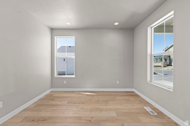 empty room with a textured ceiling and light hardwood / wood-style flooring