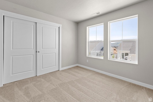 unfurnished bedroom featuring a textured ceiling, light colored carpet, and a closet