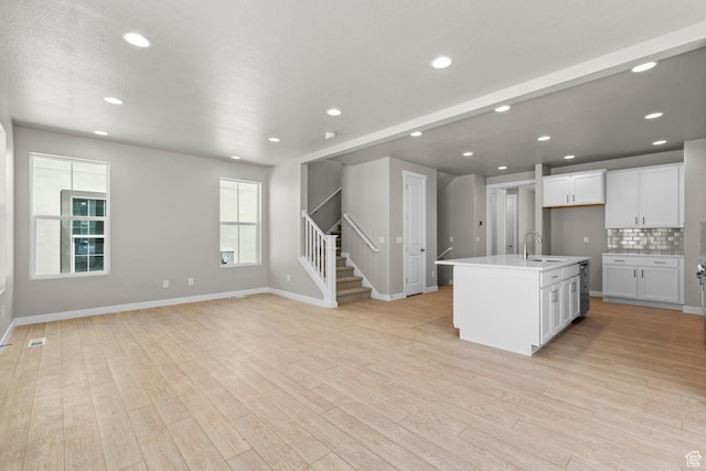 kitchen with backsplash, sink, light wood-type flooring, an island with sink, and white cabinetry